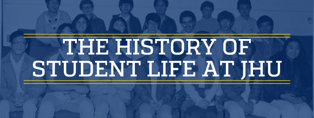 Graphic of text overlayed on a image. The text reads The History of Student Life at JHU in all caps. Behind the text a black and white photo with blue tint shows a group of Chinese and Asian students sitting on bleachers smiling.