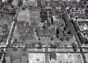 An aerial view of several buildings in the early 19th century on a gridded city block.