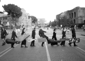 Black and white photo of seven students line up and crossing the street, all holding instrument cases in their hands.