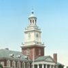 The top of Gilman Hall, visible in the photo is its uppermost floor and its clock tower, painted in white in contrast to the red brick of the rest of the building.