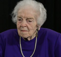 Portrait photo of Sylvia Dodd. She has white hair, wearing a blue dress, and a gold necklace.