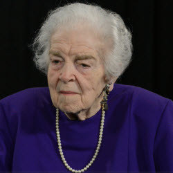 Portrait photo of Sylvia Dodd. She has white hair, wearing a blue dress, and a gold necklace.