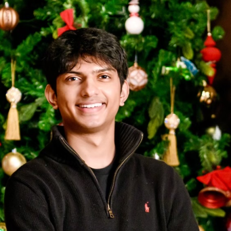 Headshot of a young man standing in front of a decorated Christmas tree.