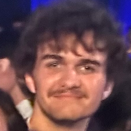 A photo of a young man standing in a crowd. He looks directly at the camera and has a slight smile.